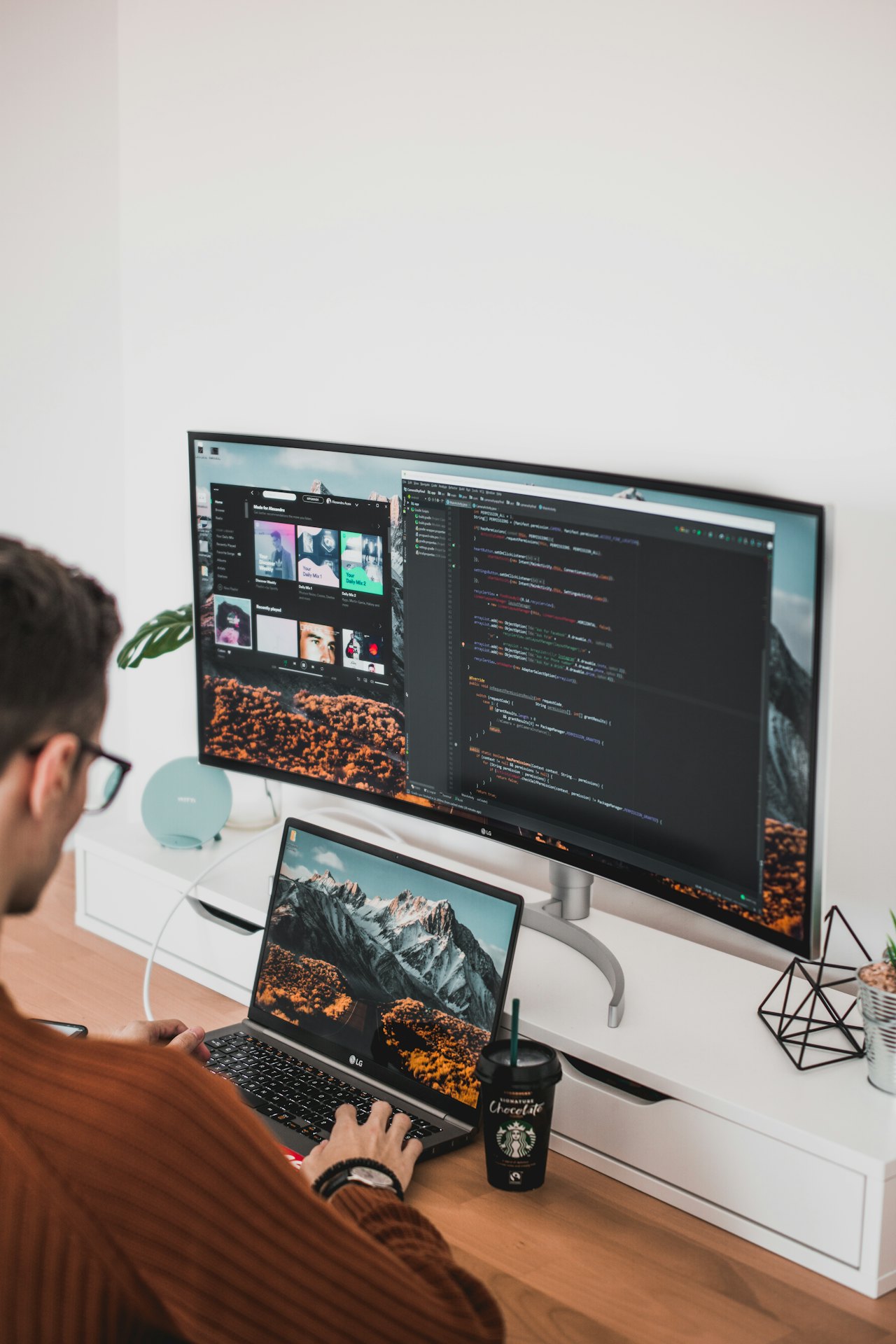 A person working at a laptop and a wide monitor